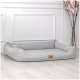 Graues Hundebett mit erhöhten Kanten und einem Lederetikett, auf einem hellen Holzboden vor einer weißen Wand platziert.