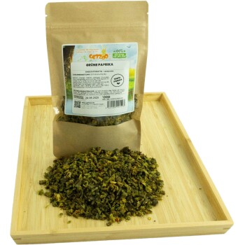 Getrocknete grüne Paprika in einem wiederverschließbaren Beutel, mit einem Etikett, das angibt, dass sie 100% frisch ist, auf einem Holztablett mit verstreuten losen Stücken.