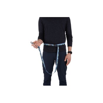 Eine Person in einem dunklen Langarmshirt hält eine bunte Hundeleine, die an einem Gürtel befestigt ist, bereit, mit einem Haustier spazieren zu gehen.