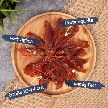Getrocknete Fleischstreifen in einem Kreis auf einem Holzbrett, beschriftet mit "Proteinquelle," "verträglich," "Größe 10-14 cm," und "wenig Fett."