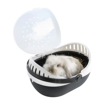 Un lapin gris et blanc duveteux est assis à l'intérieur d'un transporteur pour animaux de compagnie noir et blanc avec un couvercle transparent, entouré de foin.