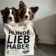 Zwei Hunde, einer braun-weiß und der andere merle, schauen aus einer beigen Tragetasche mit 'HUNDE LIEB HABER' und dem Logo von Bellfor.