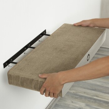 Eine Person installiert einen wandmontierten Katzenkratzbaum mit einer strukturierten Oberfläche, gehalten von einer schwarzen Metallhalterung an einer hellen Wand.