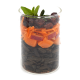 Ein klares Glasgefäß, geschichtet mit dunklen Kroketten, Karottenstreifen, gewürfelten Früchten, getrockneten Heidelbeeren und garniert mit grünen Blättern.