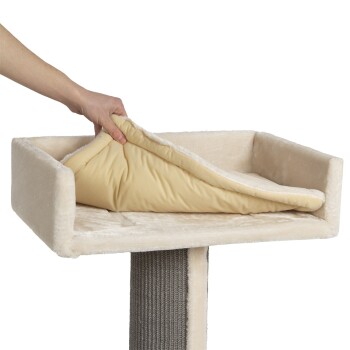 Eine Hand hebt ein abnehmbares, weiches beiges Kissen von einer plüschigen Katzenbaum-Plattform mit einer gemütlichen, cremefarbenen Oberfläche.