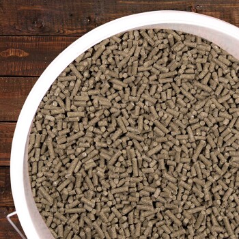 Nahaufnahme eines großen weißen Behälters, gefüllt mit kleinen, zylindrischen, braunen Tierfutterpellets, vor einem Holz-Hintergrund.