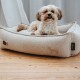 Kleiner, flauschiger cremefarbener Hund auf einem beigen Stoffbett mit "HUNTER"-Etikett und Hundesilhouette auf einem Holzboden.