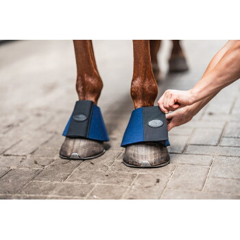 Vordere Pferdehufe in blauen Hufglocken, eine Hand befestigt die Klettlasche mit 'EQUINE'-Logo