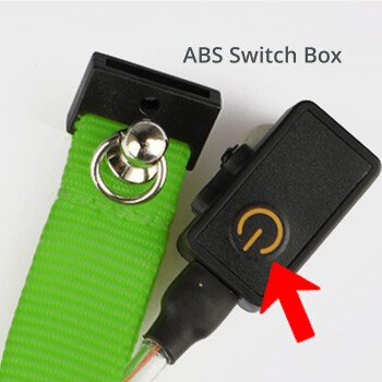Nahaufnahme eines grünen Haustierhalsbands mit einer ABS-Schaltbox, die einen Netzschalter mit der Aufschrift 'ABS Switch Box' enthält.