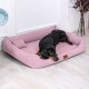 Ein schwarzer Dobermann liegt bequem auf einem rosa Hundebett mit einem kleinen Kissen, in einem hellen Raum mit Holzboden.