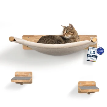 Eine getigerte Katze entspannt sich auf einer beigen Stoffhängematte, die an einer Holzwandhalterung befestigt ist, mit zwei kleinen Holzregalen darunter. Ein Etikett liest "1,3 SEHR GUT."
