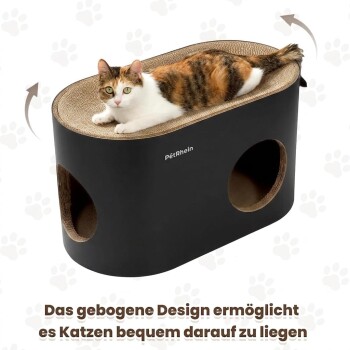 Schwarze Katze kratzt an einem ovalen schwarzen Papp-Katzenhaus/Kratzmöbel mit runden Löchern und weißem ‚Petrhein‘-Logo im Wohnzimmer.