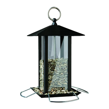 Mangeoire pour oiseaux en métal noir avec un toit en pente, remplie de graines de tournesol, et un anneau de suspension en haut.
