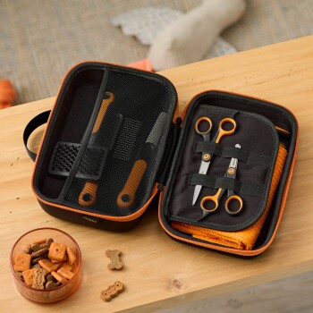 Offenes schwarz-orangefarbenes Haustierpflegeset auf Holztisch mit Schere, Kämmen, orangefarbenem Handtuch und Schale mit Hundesnacks.