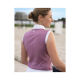Eine Frau in einem ärmellosen rosa Reitoberteil mit einem weißen Kragen steht im Freien, mit einem verschwommenen Hintergrund einer Reitarena.