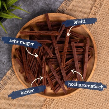 Ein Holzbrett hält dunkle, braune Leckerlis für Haustiere mit den deutschen Aufschriften: "sehr mager," "leicht," "lecker," und "hocharomatisch."