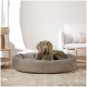Ein grauer Hund ruht sich in einem plüschigen, runden Hundebett in einem modernen Wohnzimmer mit hellen Wänden und Möbeln aus.