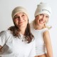 Zwei Frauen in beigen Mützen und weißen Oberteilen, die lächeln und zusammen vor einem schlichten Hintergrund posieren.