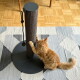 Rotgetigerte Katze kratzt an einem hohen grauen Sisalpfosten mit rundem schwarzem Sockel und hängendem Seilspielzeug auf einem gemusterten Teppich.