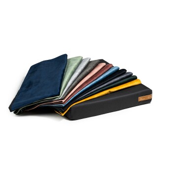 Ein Stapel bunter Haustierdecken in verschiedenen Farbtönen, darunter Marineblau, Grün, Grau und Senf, die über einem schwarzen Kissen angeordnet sind.