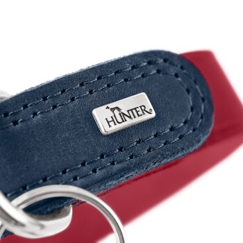 Nahaufnahme eines marineblauen Lederhundehalsbands mit rotem Futter, Metallring und 'HUNTER'-Logoschild.