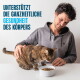 Mann streichelt eine getigerte Katze, die aus einer weißen Trockenfutterschüssel frisst; sichtbarer Text: "UNTERSTÜTZT DIE GANZHEITLICHE GESUNDHEIT DES KÖRPERS".