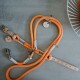 Eine orangefarbene Hundeleine aus strapazierfähigem Seil, mit Lederakzenten und Metallclips, auf einer grauen Oberfläche ausgelegt.