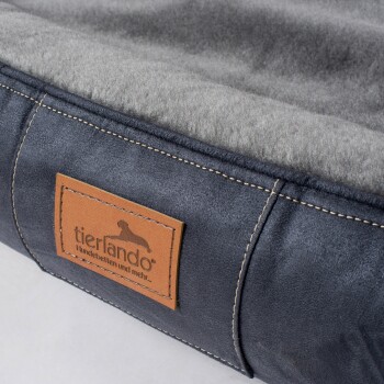 Nahaufnahme eines grauen und marineblauen Hundebetts mit einem braunen Lederetikett mit der Aufschrift "tierlando Hundebetten und mehr..."