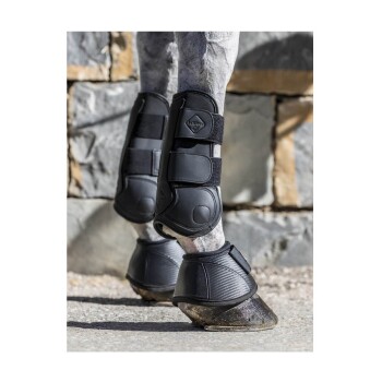 Schwarze Pferdebeinschützer an den Beinen eines Pferdes, die Schutzausrüstung vor einem Steingemäuer-Hintergrund zeigen.