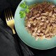 Huisdiervoeding op een lichtgroen bord met gescheurd vlees in saus, gegarneerd met peterselie, naast een gouden vork op een donker doek.