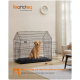 Hund sitzt in einem schwarzen Draht-Hundekäfig mit dachähnlichem Design in einem Wohnzimmer, mit Spielzeug und einer Uhr an der Wand.