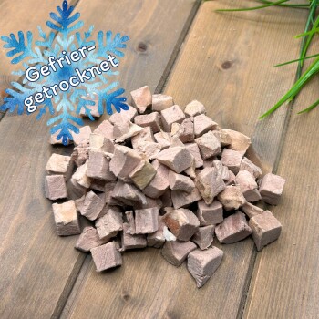 Haufen gefriergetrockneter Fleischwürfel auf einem Holzbrett mit blauem Schneeflocken-Label 'Gefrier-getrocknet'.