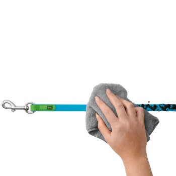 Eine Hand wischt mit einem grauen Tuch über eine blaue Hundeleine und zeigt den Clip der Leine sowie ein strukturiertes grünes Etikett.