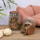 Zwei Glasbehälter mit Tierleckerlis auf einer Holzoberfläche, einer umgekippt. Ein rosa Haustierbett und zwei weiße Seilspielzeuge sind im Hintergrund.