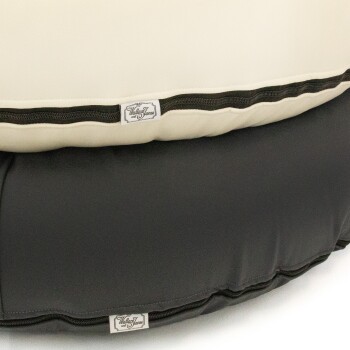 Ein Haustierbett mit einer cremefarbenen Oberseite und einem schwarzen Boden, ausgestattet mit einem Reißverschluss und einem Etikett, auf dem "Wallace und Jane" steht.