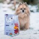 Un chien Pomeranian duveteux se tient dans la neige, avec un sac de nourriture pour chien étiqueté "WOW" au premier plan, contenant du canard, de la menthe et de la betterave.