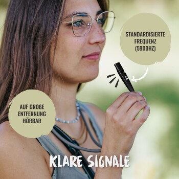 Eine Person hält eine schwarze Hundetrainingpfeife, mit einem Text, der angibt, dass sie eine standardisierte Frequenz von 5900Hz ausstrahlt und aus der Ferne hörbar ist.
