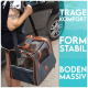 Eine tätowierte Person trägt eine robuste Tragetasche für Haustiere mit Netzpaneelen, beschriftet mit "TRAGE KOMFORT", "FORM STABIL" und "BODEN MASSIV."
