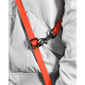 Nahaufnahme eines grauen Haustiergeschirrs mit einem leuchtend orangefarbenen Riemen und einer schwarzen Metallschnalle, die das verstellbare Design zeigt.