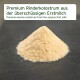 Haufen blassbeigen Kolostrumpulvers auf dunkler Oberfläche; Etikett lautet 'Premium Rinderkolostrum' und zeigt einen englischen Untertitel.