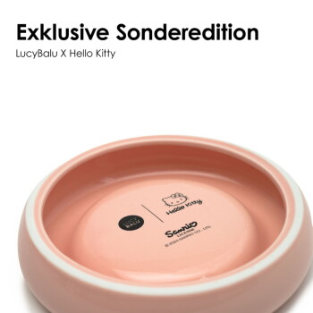 Eine graue Katze schnüffelt an einer pinken, runden Futterschüssel mit dem Text 'Schnurrhaar-freundliches Design für stressfreies Fressen' darauf.