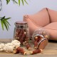 Ein Glasbehälter voller Hundeleckerlis, einschließlich gerollter Fleischstangen, ist auf einem Holztisch neben einem plüschigen rosa Haustierbett und einem Seilspielzeug umgekippt.