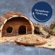 Ein Holz-Haustierhaus neben einer Schüssel mit buntem Haustierfutter, mit dem Text "Ganzjahresfütterung" in einem kreisförmigen Design darüber.