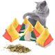 Eine verspielte graue Katze interagiert mit bunten, mit Katzenminze gefüllten Pyramidentoys in Gelb und Rot, mit getrockneter Katzenminze, die in der Nähe verstreut ist.