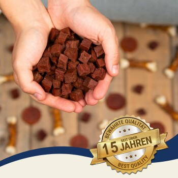 Hände, die einen Haufen kleiner, brauner Haustierleckerlis halten, mit einem Abzeichen, das 'Beste Qualität' und '15 Jahre' auf Deutsch angibt, was 15 Jahre Qualität bedeutet.