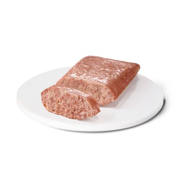 Un bloc rectangulaire de nourriture pour animaux, partiellement tranché, présenté sur une assiette blanche contre un fond uni.