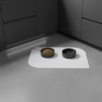 Schwarze Futter- und Wassernäpfe auf einer weißen Matte in einer modernen grauen Küchenecke.