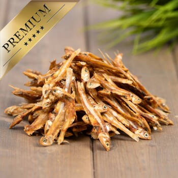 Ein Haufen getrockneter Fischleckereien für Haustiere, beschriftet "PREMIUM" in einem goldenen Banner, auf einer Holzoberfläche mit grünem Gras im Hintergrund.