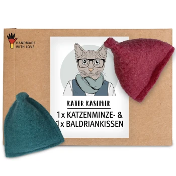Ein Karton mit einem Etikett mit dem Text "KATER KASIMIR 1 x KATZENMINZE- & 1 x BALDRIANKISSEN," neben zwei Filzspielzeugen, einem in Teal und einem in Rot.