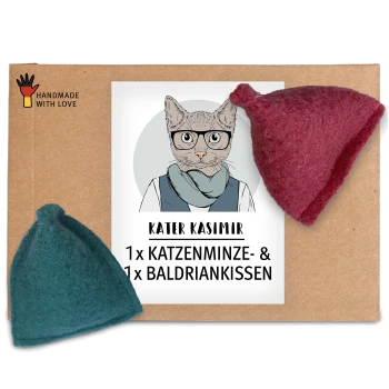 Ein Karton mit einem Etikett mit dem Text "KATER KASIMIR 1 x KATZENMINZE- & 1 x BALDRIANKISSEN," neben zwei Filzspielzeugen, einem in Teal und einem in Rot.